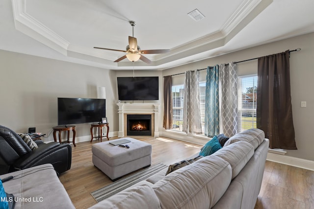 living area featuring light wood finished floors, baseboards, a raised ceiling, and crown molding