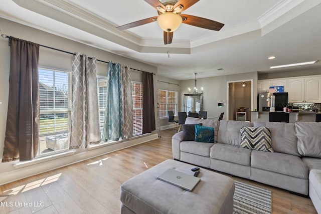 living room featuring light wood-type flooring, a tray ceiling, ornamental molding, and ceiling fan with notable chandelier