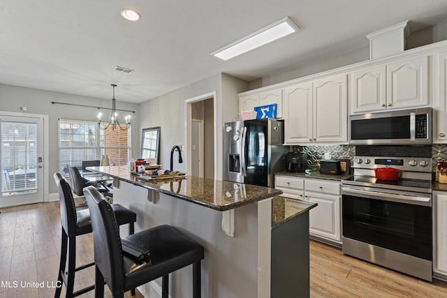 kitchen with a kitchen island, white cabinetry, appliances with stainless steel finishes, dark stone counters, and pendant lighting