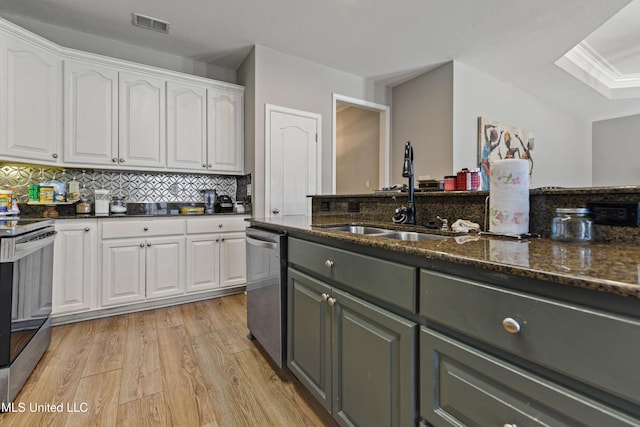 kitchen with appliances with stainless steel finishes, light wood-style floors, white cabinets, a sink, and dark stone counters