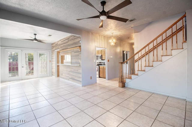 unfurnished living room featuring wood walls, ceiling fan with notable chandelier, a textured ceiling, and light tile patterned floors