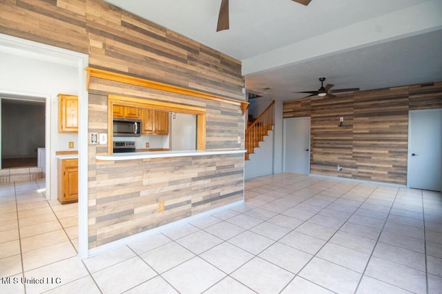 kitchen with ceiling fan, stainless steel appliances, wood walls, and light tile patterned floors