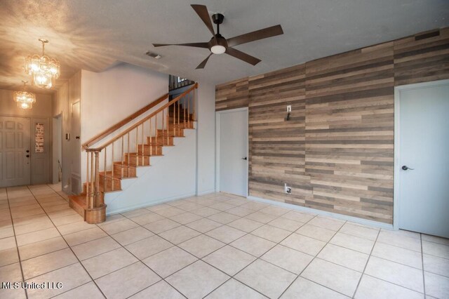 interior space with light tile patterned floors, ceiling fan with notable chandelier, and wood walls