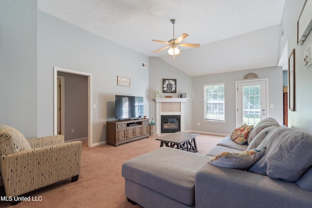 living area with light colored carpet, a ceiling fan, a glass covered fireplace, high vaulted ceiling, and baseboards