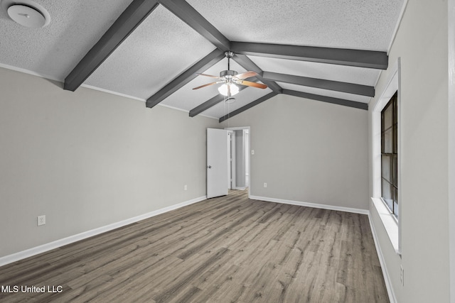 empty room with vaulted ceiling with beams, a ceiling fan, a textured ceiling, wood finished floors, and baseboards