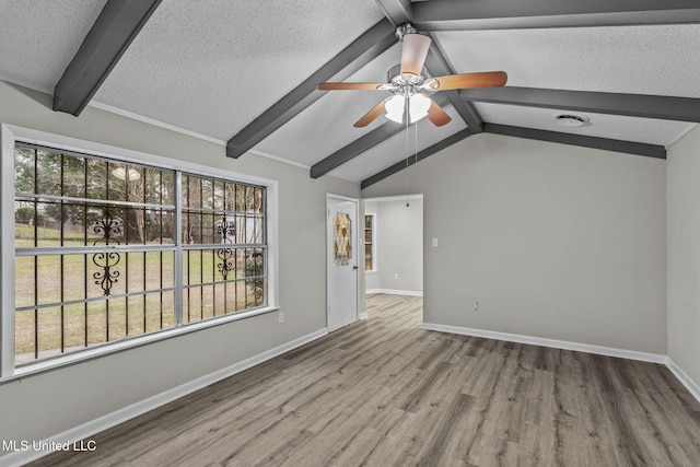 spare room with baseboards, wood finished floors, vaulted ceiling with beams, a textured ceiling, and a wealth of natural light