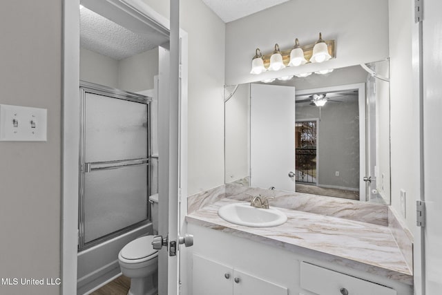 bathroom featuring a ceiling fan, toilet, combined bath / shower with glass door, a textured ceiling, and vanity