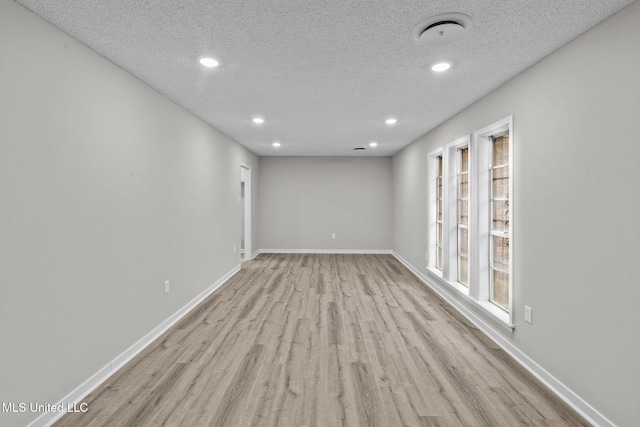 empty room featuring a textured ceiling, recessed lighting, wood finished floors, and baseboards