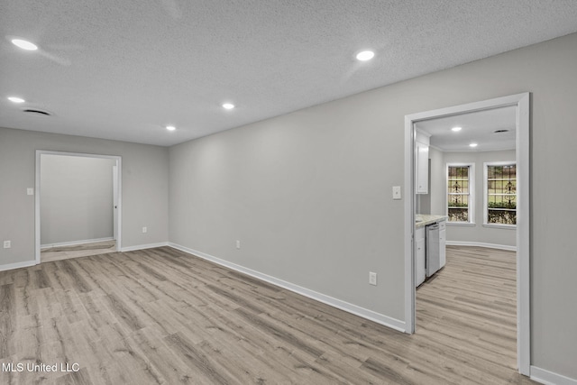 empty room featuring a textured ceiling, light wood finished floors, recessed lighting, and baseboards