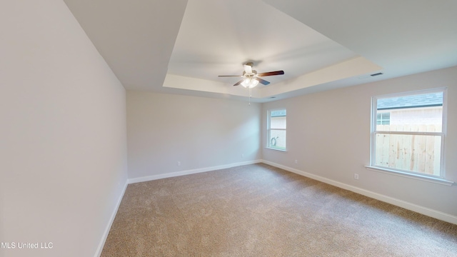 carpeted spare room with a raised ceiling and ceiling fan