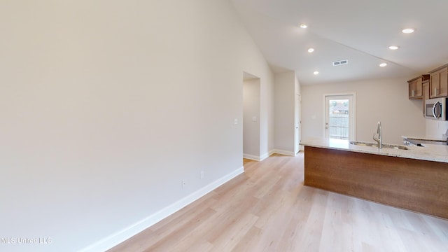 kitchen with light hardwood / wood-style floors, light stone countertops, sink, and vaulted ceiling