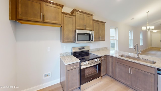 kitchen featuring light stone countertops, stainless steel appliances, sink, light hardwood / wood-style flooring, and a notable chandelier