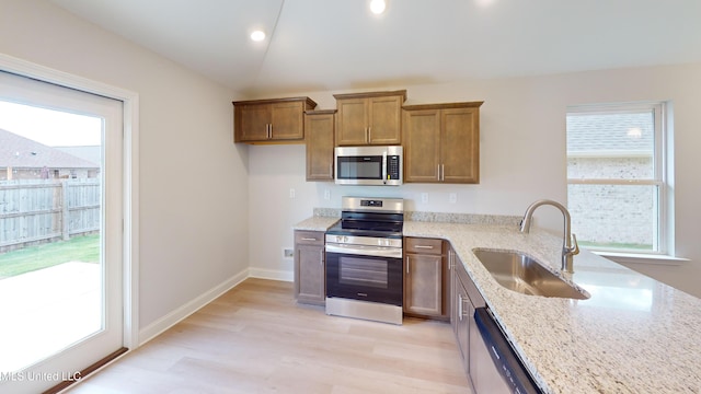 kitchen with lofted ceiling, sink, light stone countertops, light wood-type flooring, and appliances with stainless steel finishes