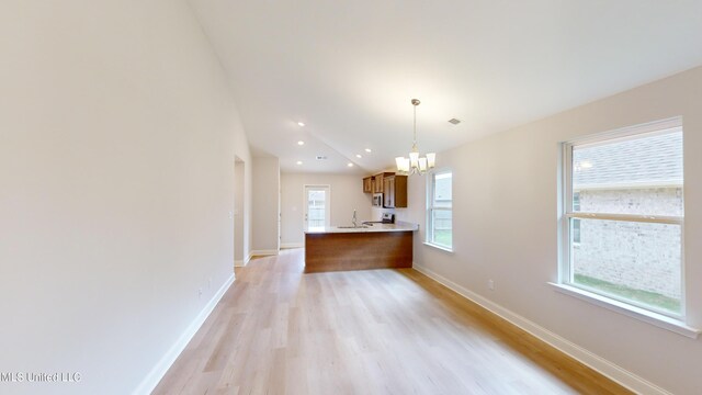 kitchen featuring kitchen peninsula, light wood-type flooring, decorative light fixtures, and an inviting chandelier