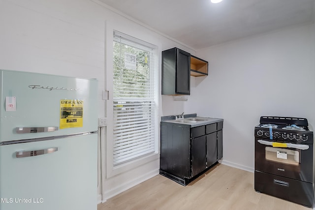 kitchen featuring light countertops, black gas range, freestanding refrigerator, a sink, and light wood-type flooring