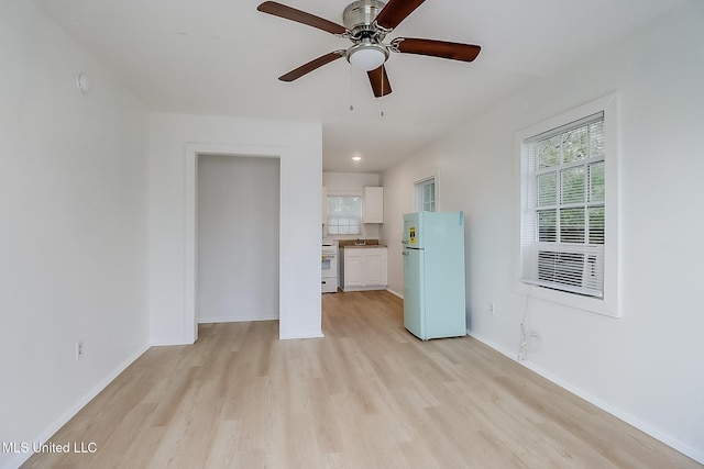 unfurnished living room with light wood-type flooring, a sink, ceiling fan, and baseboards