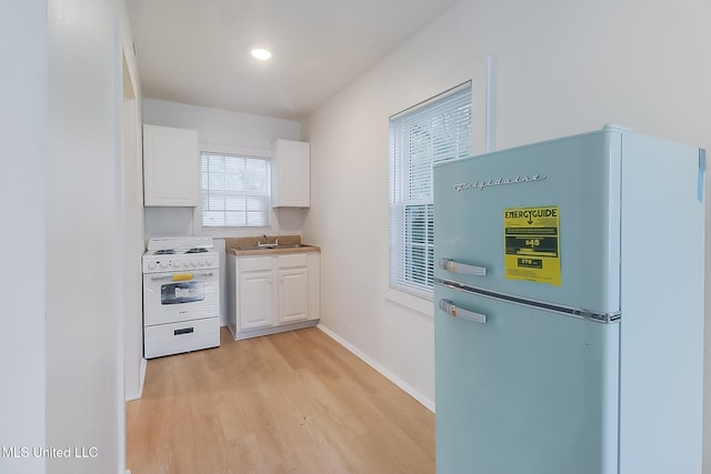 kitchen with light wood-type flooring, freestanding refrigerator, electric stove, and white cabinets