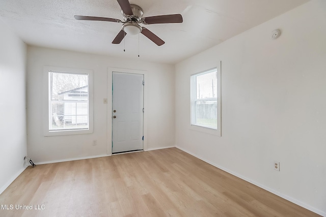 empty room featuring light wood-style floors, a textured ceiling, baseboards, and a ceiling fan