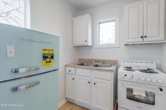 kitchen with electric range, a sink, white cabinetry, light countertops, and freestanding refrigerator