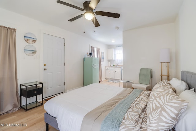 bedroom featuring freestanding refrigerator, light wood-style flooring, ensuite bathroom, and a ceiling fan