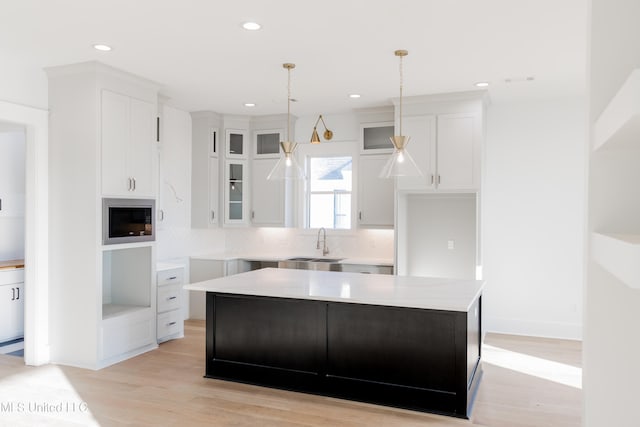 kitchen featuring built in microwave, sink, light hardwood / wood-style flooring, white cabinets, and a center island