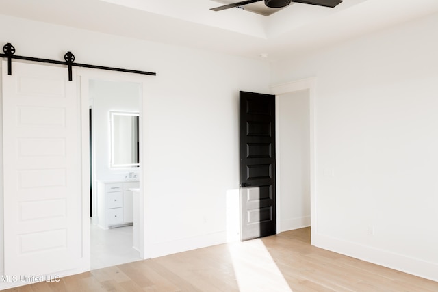 unfurnished room with a barn door, light hardwood / wood-style flooring, and ceiling fan