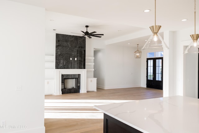 unfurnished living room featuring ceiling fan, a large fireplace, light wood-type flooring, and french doors