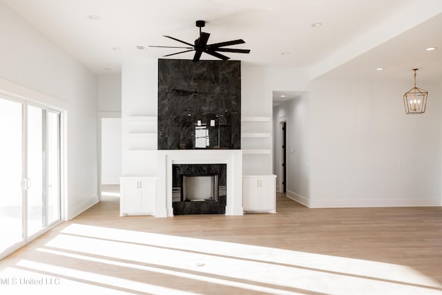 unfurnished living room with ceiling fan, light wood-type flooring, a fireplace, and built in shelves