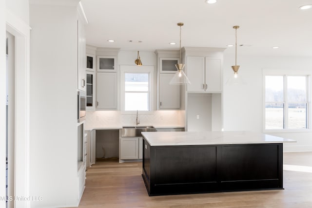 kitchen featuring white cabinets, sink, hanging light fixtures, decorative backsplash, and a kitchen island