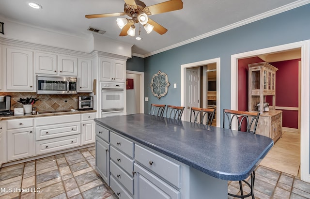 kitchen with a kitchen breakfast bar, visible vents, white double oven, stainless steel microwave, and white cabinetry