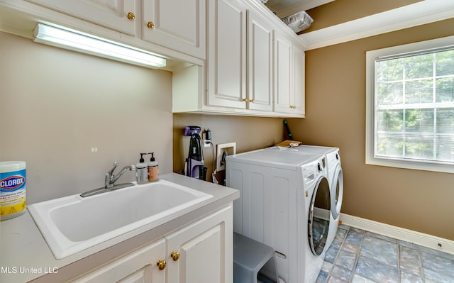 clothes washing area featuring independent washer and dryer, cabinet space, a sink, baseboards, and stone finish flooring