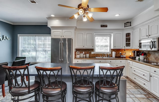kitchen featuring a kitchen breakfast bar, ceiling fan, appliances with stainless steel finishes, a sink, and white cabinetry
