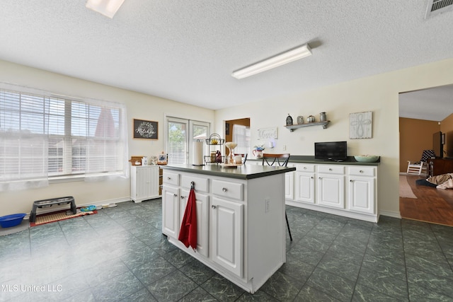 kitchen featuring dark countertops, a textured ceiling, a center island, white cabinetry, and visible vents