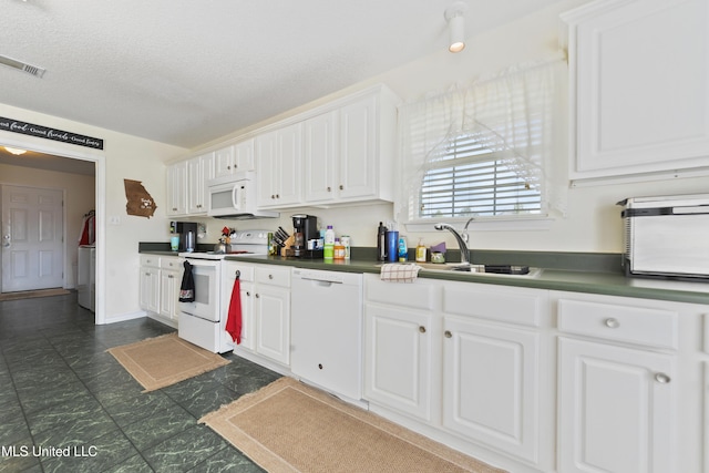 kitchen with visible vents, dark countertops, a sink, white cabinets, and white appliances