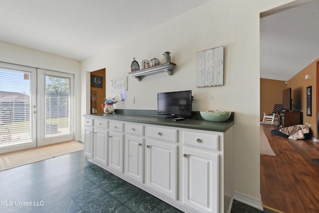 kitchen with baseboards, a textured ceiling, white cabinets, and dark countertops