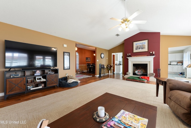living area with visible vents, lofted ceiling, wood finished floors, a tile fireplace, and a ceiling fan