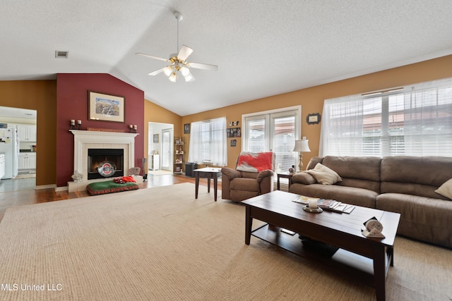 living area featuring visible vents, a textured ceiling, a tile fireplace, a ceiling fan, and vaulted ceiling