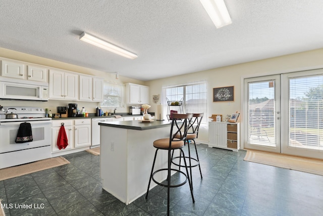 kitchen featuring white appliances, a kitchen breakfast bar, white cabinets, and a kitchen island