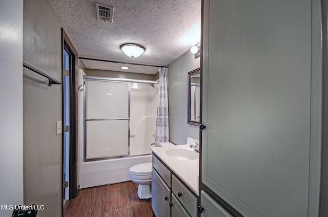 full bathroom with hardwood / wood-style floors, combined bath / shower with glass door, a textured ceiling, toilet, and vanity