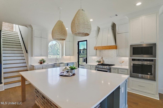 kitchen with a center island, white cabinets, pendant lighting, custom exhaust hood, and appliances with stainless steel finishes