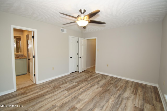 unfurnished bedroom with ensuite bathroom, a textured ceiling, a closet, ceiling fan, and light hardwood / wood-style flooring