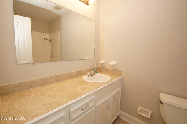 bathroom with toilet, vanity, and a tile shower