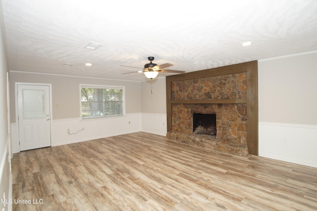 unfurnished living room featuring ceiling fan, a textured ceiling, light hardwood / wood-style flooring, ornamental molding, and a fireplace