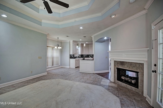 living room featuring a tiled fireplace, crown molding, a raised ceiling, and ceiling fan with notable chandelier