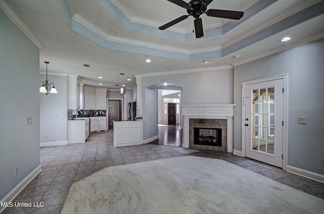 unfurnished living room featuring crown molding, sink, ceiling fan with notable chandelier, and a fireplace