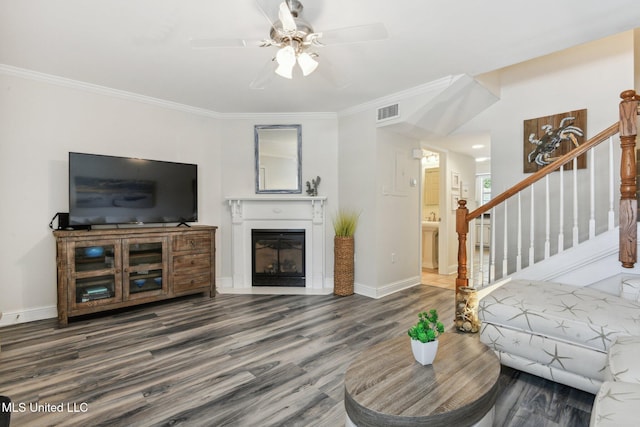 living area featuring stairway, ornamental molding, a glass covered fireplace, wood finished floors, and baseboards