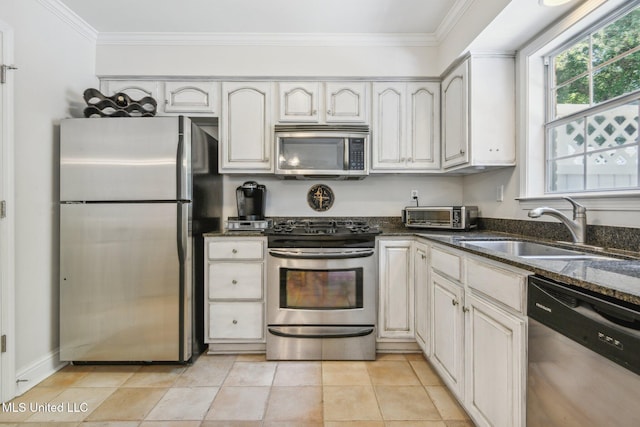 kitchen with light tile patterned floors, dark stone counters, appliances with stainless steel finishes, ornamental molding, and a sink