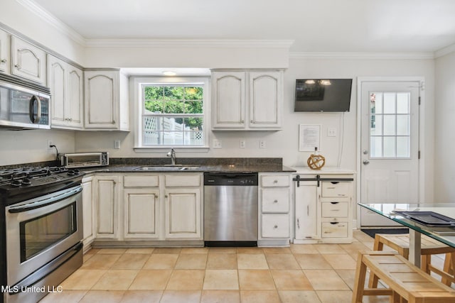 kitchen featuring light tile patterned floors, appliances with stainless steel finishes, cream cabinets, crown molding, and a sink