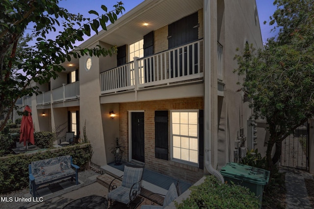 back of house with brick siding, a patio area, and a balcony