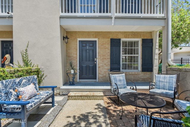 entrance to property with brick siding, a balcony, and stucco siding